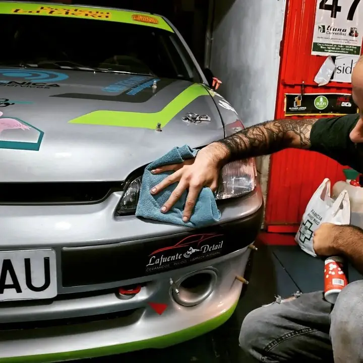 Detallista puliendo el faro de un coche de rally plateado con vinilos verdes en el taller