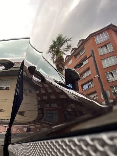 Reflejos nítidos de edificios y una palmera en la pintura negra de un Porsche Macan tras el pulido