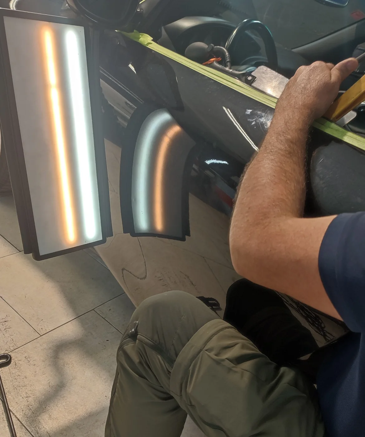 Reparación de una abolladura en la chapa de un coche, con una lámpara de reflejos y una herramienta